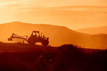 Fototapeta premium Tractor in a farm field at sunset. Backlight warm tones.
