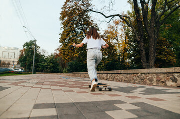 Fototapeta premium View from the back, a woman rides a longboard, pushes off the ground, photo in motion. Woman skater walks on a longboard around the city