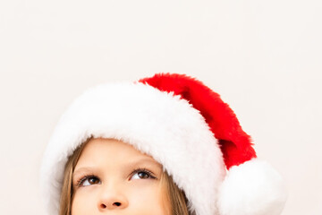 A cute little girl in a red Christmas hat looks up.