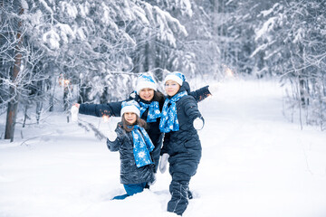 Fototapeta na wymiar Smiling young girls and there mother with sparklers in hands. Happy winter time in the forest. The girls are in a dark coat, blue Santa Claus hat, scarf and mittens. Family christmas new year.