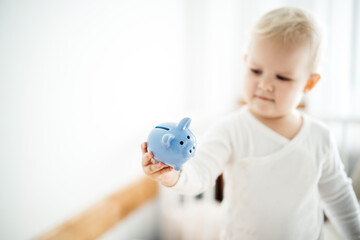 Fototapeta na wymiar small child holds a piggy bank in his hand on a light background in his room. Business and savings for the future.
