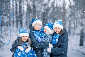 Portrait of a happy family of mother and  her children in a winter decorated forest. The girls are in a dark coat,  blue  Santa Claus hat, scarf and mittens. Family christmas new year.