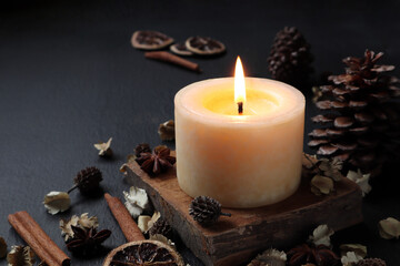nice aromatic scented candle pillar lighting on the wooden holder on black wooden table with dried flowers , herbs and spices pinecone in the living room during Christmas new year party happy family