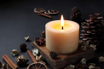 Fototapeta na wymiar nice aromatic scented candle pillar lighting on the wooden holder on black wooden table with dried flowers , herbs and spices pinecone in the living room during Christmas new year party happy family