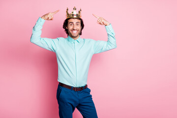 Photo portrait of excited guy pointing two fingers at crown on head isolated on pastel pink colored...