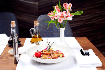 Meat dish, oil and flowers on the table