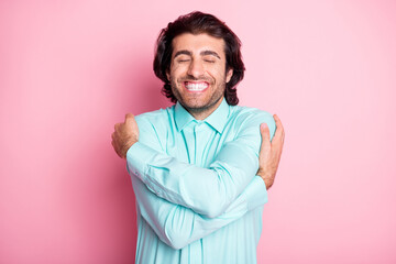 Photo portrait of happy guy hugging himself isolated on pastel pink colored background