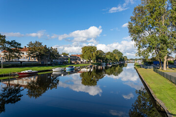 Boats moored on the side of the Oegstgeester canal in the South-Holland village of Rijnsburg in the Netherlands. On a cloudy and sunny day.