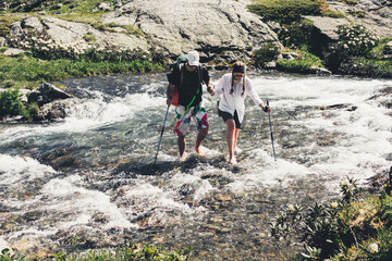 Tourists with ski poles cross the stormy mountain stream while traveling in the mountains