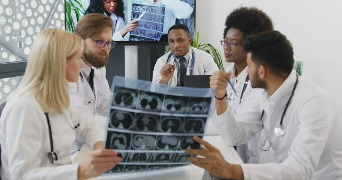 Good-looking confident purposeful high-skilled multiracial doctors advising about the treatment of patient using x-ray scan during meeting in office room,front view