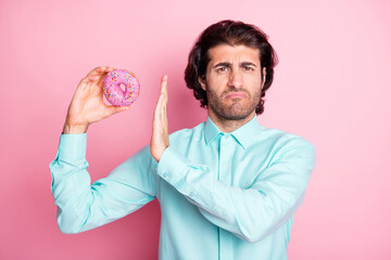 Photo of negative attitude arab guy hold round donut cake avoid eating sweets isolated pink color...