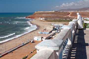 Mężczyzna w muzułmańskim stroju stoi przy barierce na klifie i patrzy  na morze. © Miroslaw