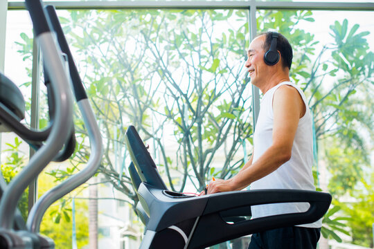 Happy Senior Asian Man Running On A Treadmill In Gym.