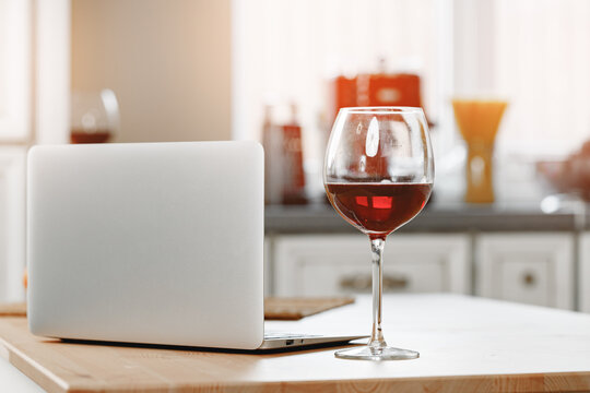 Laptop and glass of red wine on wooden kitchen table