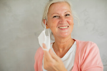 Portrait of senior woman taking off protective medical mask for protection from virus