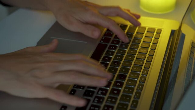 Two hands typing very fast on a computer keyboard at night.