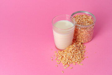 Oat milk in glassware and dry oat flakes on pink background