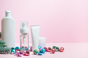 Christmas beauty skin care cosmetic products with decoration balls on the pink background.