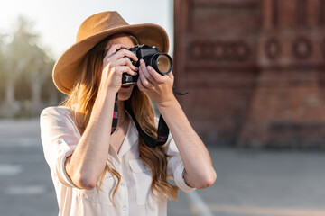 Beautiful woman in explorer outfit traveling and taking pictures with vintage camera. Freelance photographer working outdoors in Barcelona.