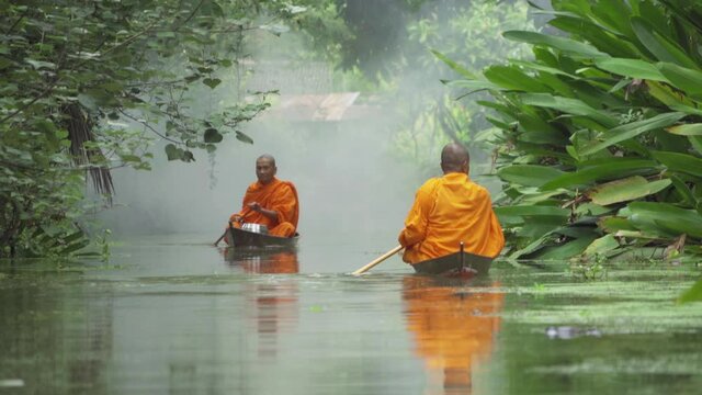 Local Thai monks with alms. Men sailing wooden boat in canal or river for receiving food, Traditional Thai Buddhism lifestyle. Asia, Thailand.