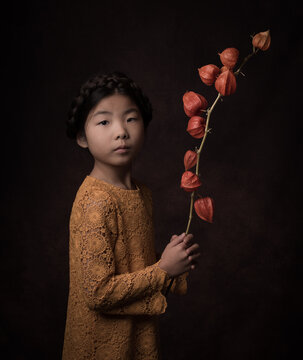 Studio portrait of young girl holding a branch of  an orange lantern flower, in Rembrandt style (Cape gooseberry, Physalis alkekengi )	
