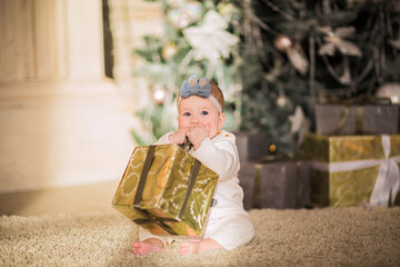 Baby girl posing with a gift sitting on a floor against Christmas back.