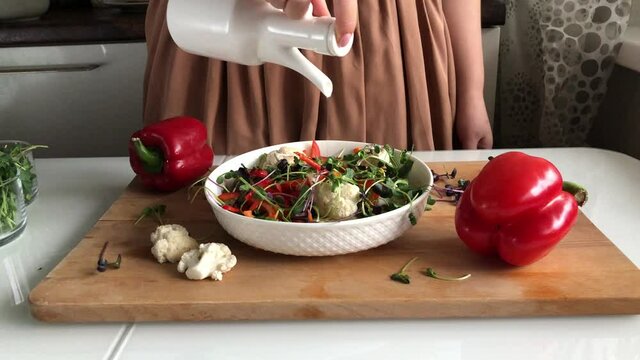 The girl pours olive oil into a beautiful delicious salad with vegetables and sprouts