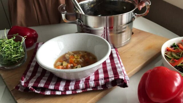 Pouring soup from a pot into a plate using a ladle
