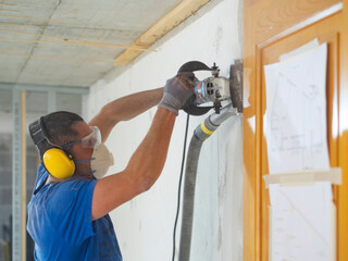 worker smoothes the wall with machinery with mask..