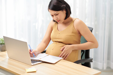 Obraz premium Tired pregnant woman working