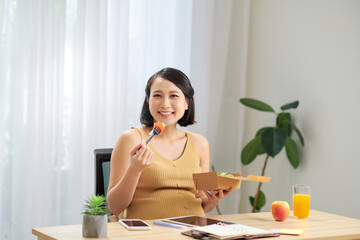 A young pregnant woman standing in home office and using tablet pc. Breakfast time.