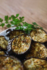 Eggplant baked with spices on plate with with bunch of parsley on wooden table, close-up view, selective shallow focus