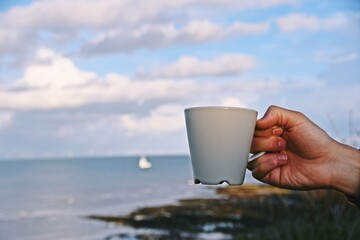 Cup of coffee in the hand on the sky and sea background. Good morning, world!