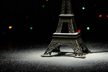 Miniature of the Eiffel Tower. Snow around the Eiffel Tower in Paris. In the dark - a ray of light from above and against the background of shining garlands. Eiffel Tower in the New Year. Macro. 