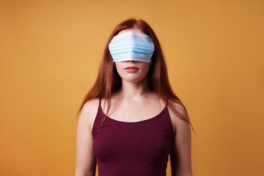 young woman wearing medical face mask over her eyes - funny corona denier concept