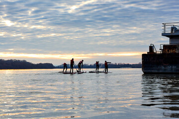 Children on SUP row in the winter Danube river at sunset