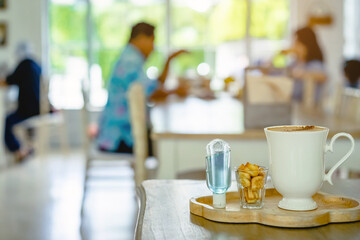 Mini portable alcohol gel bottle to kill Corona Virus(Covid-19) and biscuits and coffee cup on table with blurred image of a family eating at restaurant in background. Health care concept.