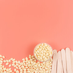 Cosmetology pink background. Hot wax granules and wooden depilatory spatulas. Top view, beauty...