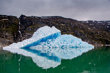 Bluish iceberg in a green sea with mountains in the background