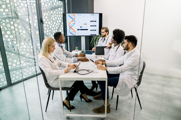 Team of diverse multiethnic medical experts or scientists, examining patient's medical record, discussing about results of clinical trial of medicines, working on reports at light modern office