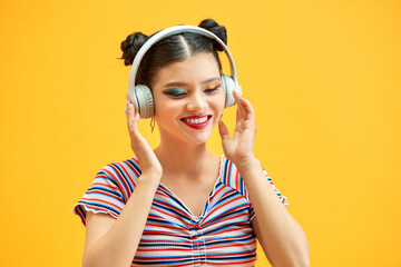 Image of young beautiful woman posing isolated over yellow background listening music with headphones.