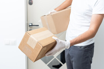 Courier, delivery man in medical latex gloves and mask safely delivers online purchases in white box to the door during the coronavirus epidemic, COVID-19. Stay home, safe concept.