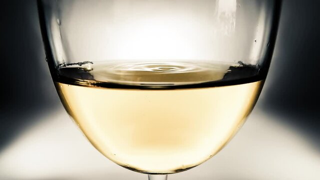 Creative macro slow motion video of white wine in a glass and a falling drops of wine. A glass with a slowly falling drops of wine close-up. Old retro grunge vintage style soft faded.