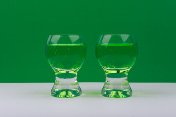 Two glasses of sparkling green drink on white table with green background