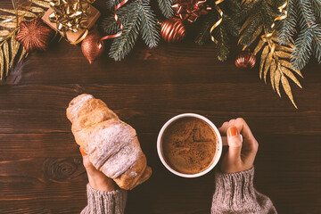 Christmas breakfast, female hands holding fresh croissant and cup of coffee