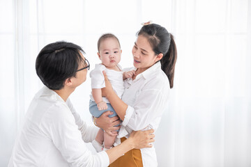 Obraz premium Smiling asian father and mother holding their baby son at home. Proud asia mother and father with daughter infant on white background. family people happy concept
