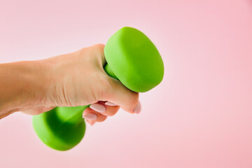 Weight loss, female fitness and healthy lifestyle concept. Woman's hand holds a dumbbell on a pink background.