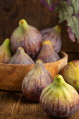 Top view of wooden bowl with figs and purple gynura leaves, with selective focus, on wooden background, vertical