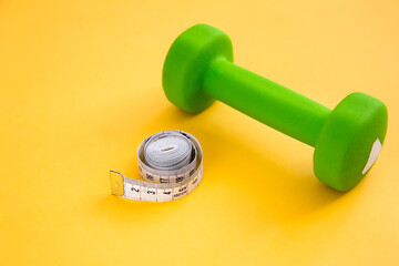 Obraz na płótnie Canvas Diet, weight loss and overweight concept. Dumbbell and measuring tape on a yellow background. Place for your text.