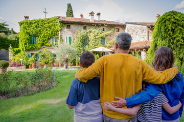 Back view of happy family hugging is standing outside their new house - This photo canuse for family, father, mother and home concept